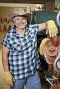 Portrait of a happy mature cowboy standing by saddle in feed store