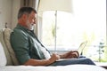 Portrait of happy mature man in casual clothes using laptop lying on sofa in house. Royalty Free Stock Photo