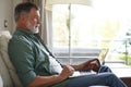 Portrait of happy mature man in casual clothes using laptop lying on sofa in house. Royalty Free Stock Photo