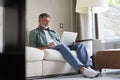Portrait of happy mature man in casual clothes using laptop lying on sofa in house. Royalty Free Stock Photo
