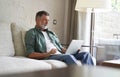 Portrait of happy mature man in casual clothes using laptop lying on sofa in house. Royalty Free Stock Photo