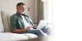 Portrait of happy mature man in casual clothes using laptop lying on sofa in house. Royalty Free Stock Photo