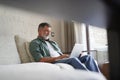 Portrait of happy mature man in casual clothes using laptop lying on sofa in house. Royalty Free Stock Photo