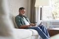 Portrait of happy mature man in casual clothes using laptop lying on sofa in house. Royalty Free Stock Photo