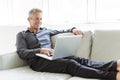 Portrait of happy mature man using laptop lying on sofa in house Royalty Free Stock Photo