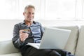 Portrait of happy mature man using laptop lying on sofa in house Royalty Free Stock Photo