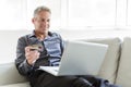 Portrait of happy mature man using laptop lying on sofa in house Royalty Free Stock Photo