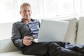 Portrait of happy mature man using laptop lying on sofa in house Royalty Free Stock Photo