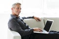 Portrait of happy mature man using laptop lying on sofa in house Royalty Free Stock Photo