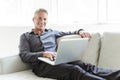 Portrait of happy mature man using laptop lying on sofa in house Royalty Free Stock Photo