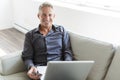 Portrait of happy mature man using laptop lying on sofa in house Royalty Free Stock Photo