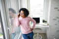 Portrait of happy mature woman making a phone call indoors, looking out of window. Royalty Free Stock Photo