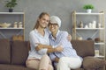 Portrait of happy mature woman together with daughter or granddaughter sitting on sofa