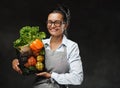 Portrait of a happy middle-aged woman in apron holds a basket of fresh vegetables and fruit Royalty Free Stock Photo