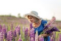 Portrait of happy middle-aged woman in hat on a flowering lupine field.