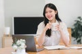 Portrait of a happy millennial Asian businesswoman holding a cup of coffee while working remotely in her home office. Royalty Free Stock Photo