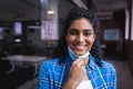 Portrait of happy mixed race businesswoman taking off face mask standing in corridor in office Royalty Free Stock Photo