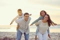 Portrait of a happy mixed race family standing and having fun together on the beach. Parents giving their children a Royalty Free Stock Photo
