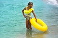 Portrait of happy modern child in yellow swimwear with yellow inflatable lifebuoy on the seashore