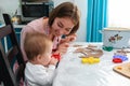 Portrait of happy mother and daughter, the girl holding the cookie cutters. Baby chewing a cookie cutter. Side view Royalty Free Stock Photo