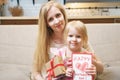 Portrait of a happy mother and daughter holding a card and a gift sitting on the sofa at home. Mother`s day concept Royalty Free Stock Photo