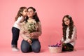 Portrait of happy mother and daughters with bouquet of white flowers isolated on pink. Daughter kissing mother. Little Royalty Free Stock Photo