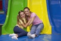 Portrait of happy mother and her teen daughter hugging near colorful slide at indoor entertainment centre for kids