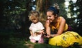 Happy mother with small daughter outdoors in summer nature, resting in forest.