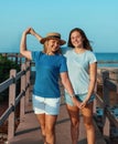 Portrait of happy mother and teenage daughter standing on pier at sea coast, holding hands and smiling, t-shirts mockup Royalty Free Stock Photo