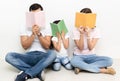 Portrait of happy multiethnic family sitting on the floor hiding behind colorful book at home. Family and childhood concept Royalty Free Stock Photo