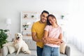 Portrait of happy multiracial couple hugging and smiling at camera, their adorable pet dog sitting on couch nearby Royalty Free Stock Photo