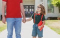 Portrait of happy nerd pupil holding teachers hand. American father and son walking trough school park. Royalty Free Stock Photo