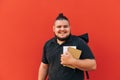 Portrait of happy overweight student on red background, wearing dark clothes, standing with books and notebook in hands and Royalty Free Stock Photo