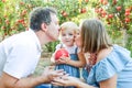 Portrait of happy parents kissing their baby girl daughter holding pomegranate fruit in sunset garden. Harvest, Family vacation an Royalty Free Stock Photo