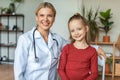 Portrait of happy pediatrician and pretty child girl looking and smiling at camera, sitting in doctor's office