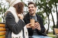 Portrait of happy people man and woman 20s drinking takeaway coffee from paper cups, while sitting on bench in green park Royalty Free Stock Photo