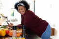 Portrait of happy plus size african american woman using smartphone, preparing food in kitchen Royalty Free Stock Photo