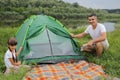 Portrait of happy positive family on vacation sets up a tent in nature near the river, attractive man with his daughter having
