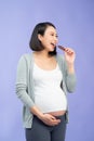 Portrait of happy pregnant woman with chocolate bar standing over purple Royalty Free Stock Photo