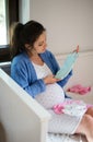 Portrait of happy pregnant woman indoors at home, holding baby clothes. Royalty Free Stock Photo