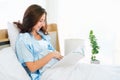 Happy pregnant woman sitting on bed reading book at home Royalty Free Stock Photo