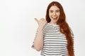 Portrait of happy pretty redhead girl laughing, pointing finger left and smiling pleased, showing something interesting Royalty Free Stock Photo