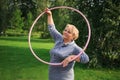 Portrait of happy pretty senior woman exercising with colorful hula hoop on nature background Royalty Free Stock Photo