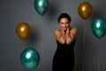 Portrait of happy pretty woman in evening black dress smiling with beautiful toothy smile posing against air balloons on gray wall Royalty Free Stock Photo