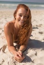 Young Caucasian woman in bikini lying on the sand and looking at camera on the beach