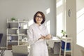 Portrait of happy doctor standing in exam room, holding clipboard and smiling at camera Royalty Free Stock Photo