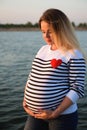 Portrait of a happy and proud pregnant woman by the river at sunset.