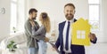 Real estate agent holding paper home and smiling standing in new house with happy clients Royalty Free Stock Photo