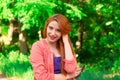 Portrait of happy red head confident young woman looking at camera smiling with red long hair isolated green trees park background Royalty Free Stock Photo