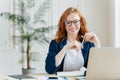 Portrait of happy redhaired woman employee in optical glasses, has satisfied expression, works with modern gadgets, waits for Royalty Free Stock Photo